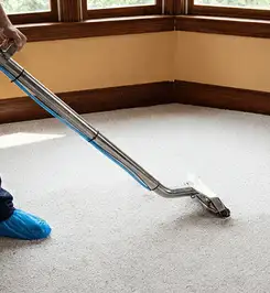 Steam carpet cleaning technician using a hot-water extraction wand on a residential carpet, wearing blue protective shoe covers Savannah, GA.