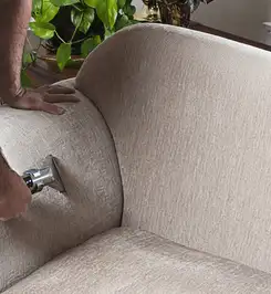 Professional upholstery cleaner deep-cleaning a fabric sofa with a handheld extraction tool and hose Savannah, GA.
