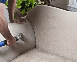 Professional upholstery cleaner deep-cleaning a fabric sofa with a handheld extraction tool and hose in Savannah, GA.